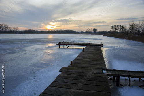 Wooden jetty  frozen lake and sunset