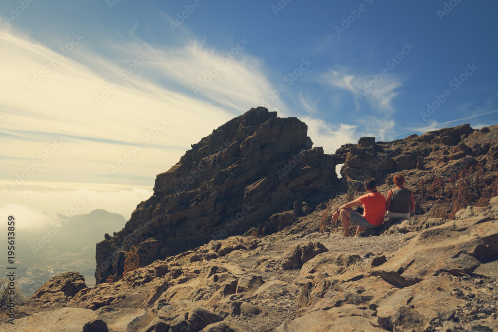 Fototapeta premium Two mature tourists sitting on rocky mountains of Gran Canaria island.