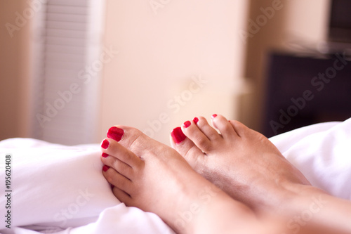 Feet of woman with red painted nails on the bed