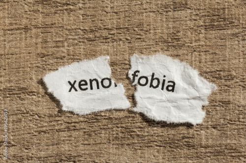 Photos Torn paper written xenofobia, portuguese and spanish word for xenophobia, over wood table