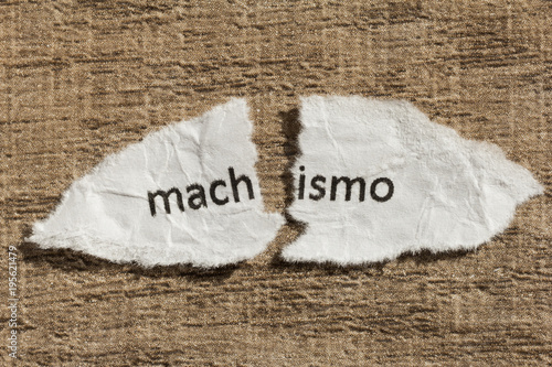 Torn paper written machismo, portuguese and spanish word for chauvism, over wood table. Concept of old and abandoned idea or practice. photo