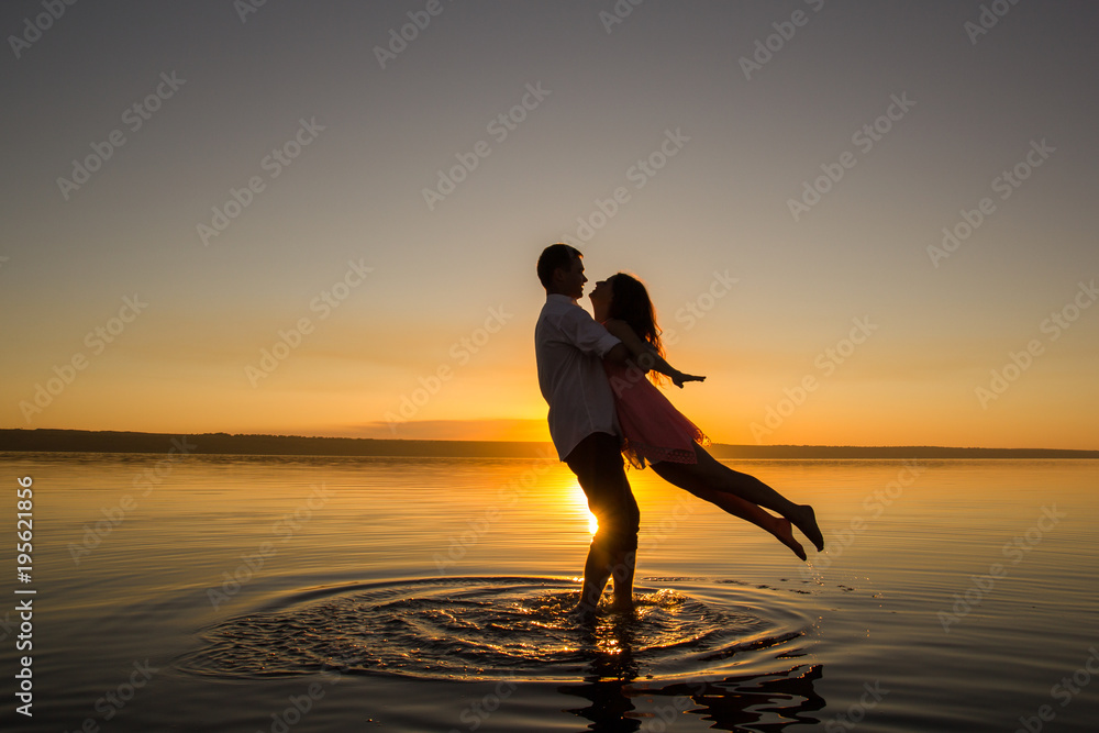 Young couple is dancing in the water on summer beach. Sunset over the sea.Two silhouettes against the sun. Calm and still surface of water. Romantic love story. Man and woman in love in honeymoon trip