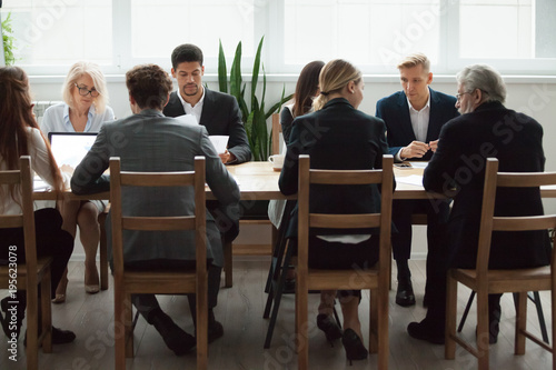 Serious multi-ethnic business people team sitting at conference table, senior executives working together with young managers at office staff meeting, focused group negotiations or teamwork concept