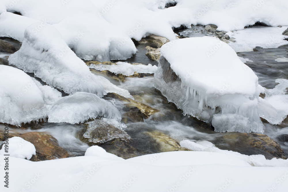 Frozen alpine river in winter in slow motion. Stones covered with frost and snow