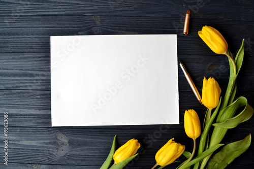 Fototapeta Naklejka Na Ścianę i Meble -  White paper, female accessories and yellow tulips on a blue vintage desk. Stylish spring still life.