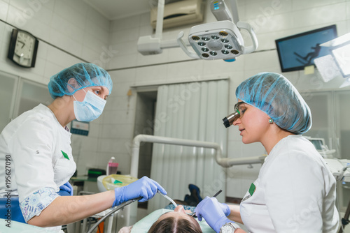 Woman at dentist clinic gets dental treatment to fill a cavity in a tooth. Dental restoration and composite material polymerization with UV light and laser. The doctor works with an assistant.