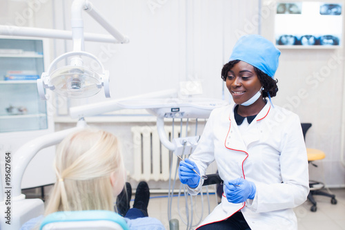 young black girl doctor dentist treats white girl's teeth.