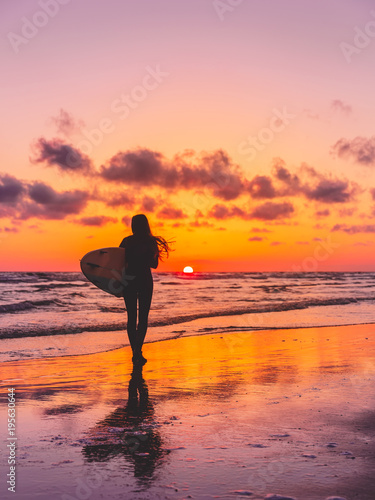 Canvas Print Silhouette of the surfer girl with surfboard on a beach at sunset