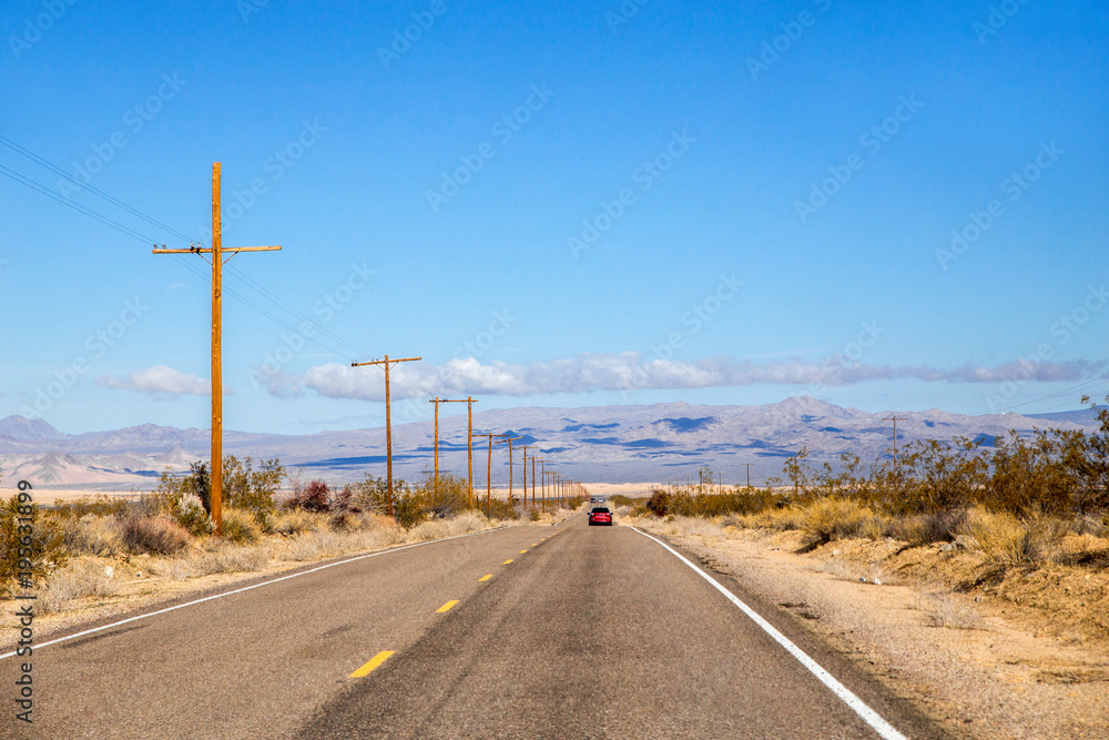 Three cars travelling along a narrow highway with mountains in the background in a spring desert landscape