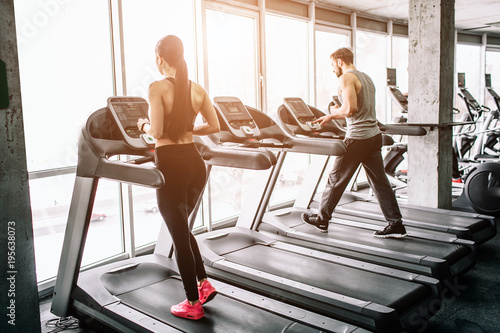 A small view of big sport room where two people are having workout. They are running on elliptical machines. The exercise is intensive and hard.