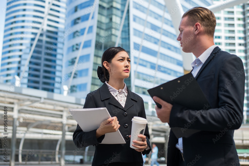 Asian business woman wear suit holding document file and plastic mug on hand talk about business future with Caucasian businessman in the city. Asian business woman wear suit holding document file and plastic mug on hand talk about business future with Caucasian businessman in the city.