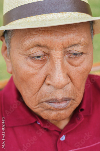 Sad old latin man wearing hat in the summer park.