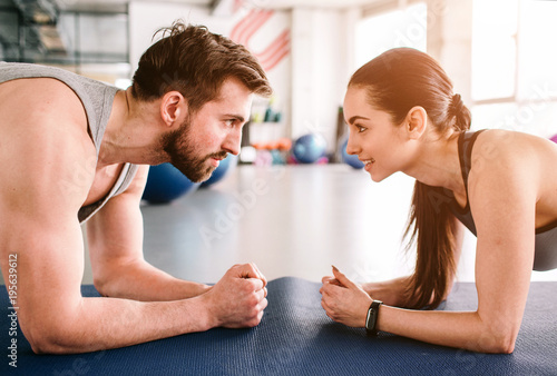 Close up of trainer and his student doing plank exercise together at the same time. They are concentrated on workout and looking at each other. Cut view.