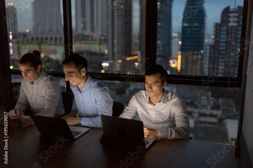 Tableau sur toile Business people team working late night in low light from laptop screen with cityscape blurred background
