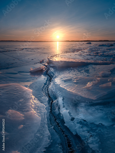 Crack in the sea ice leading towards golden sunset at winter