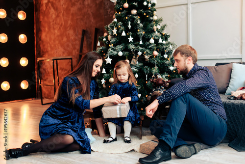 young mother and father and their little daughter in a New Year decor with gifts and a Christmas tree photo