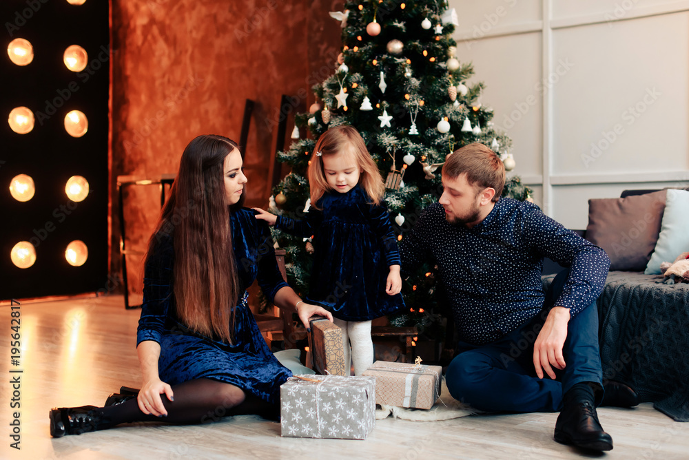 young mother and father and their little daughter in a New Year decor with gifts and a Christmas tree young mother and father and their little daughter in a New Year decor with gifts and a Christmas tree