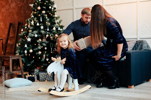 young mother and father and their little daughter in a New Year decor with gifts and a Christmas tree photo