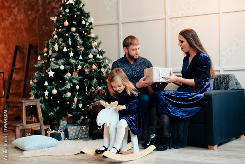 young mother and father and their little daughter in a New Year decor with gifts and a Christmas tree photo