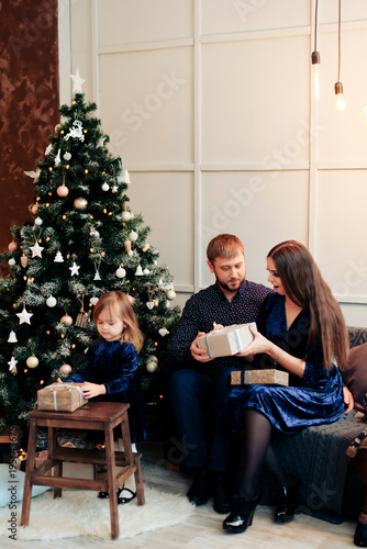 young mother and father and their little daughter in a New Year decor with gifts and a Christmas tree photo