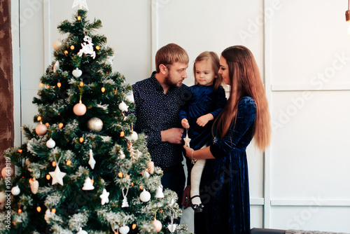 young mother and father and their little daughter in a New Year decor with gifts and a Christmas tree