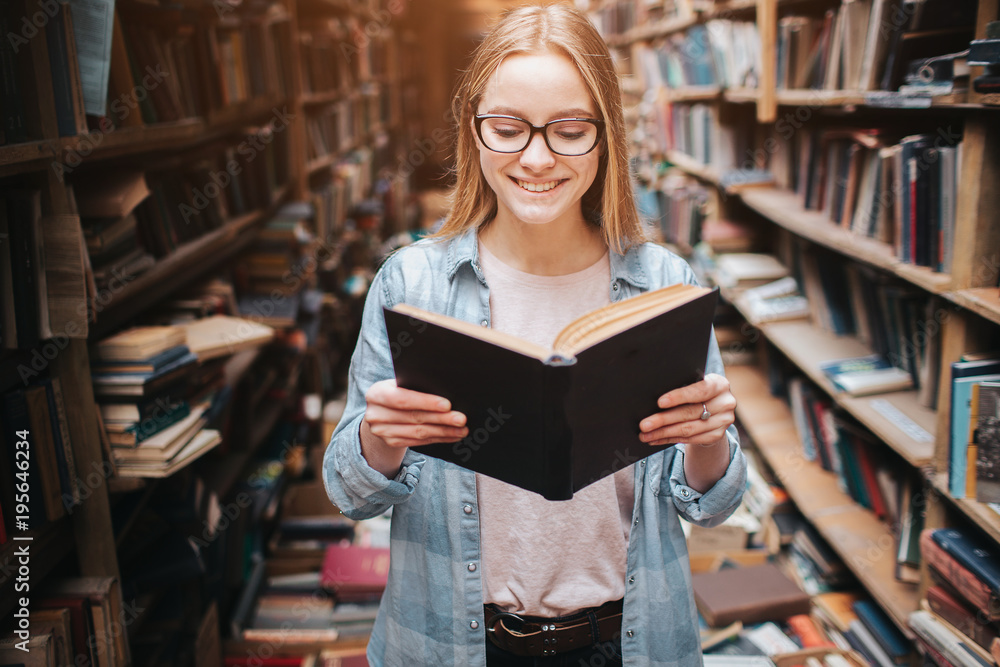 Bright and warm picture of clever student reading a book. Girl is smiling and continue to read book further.