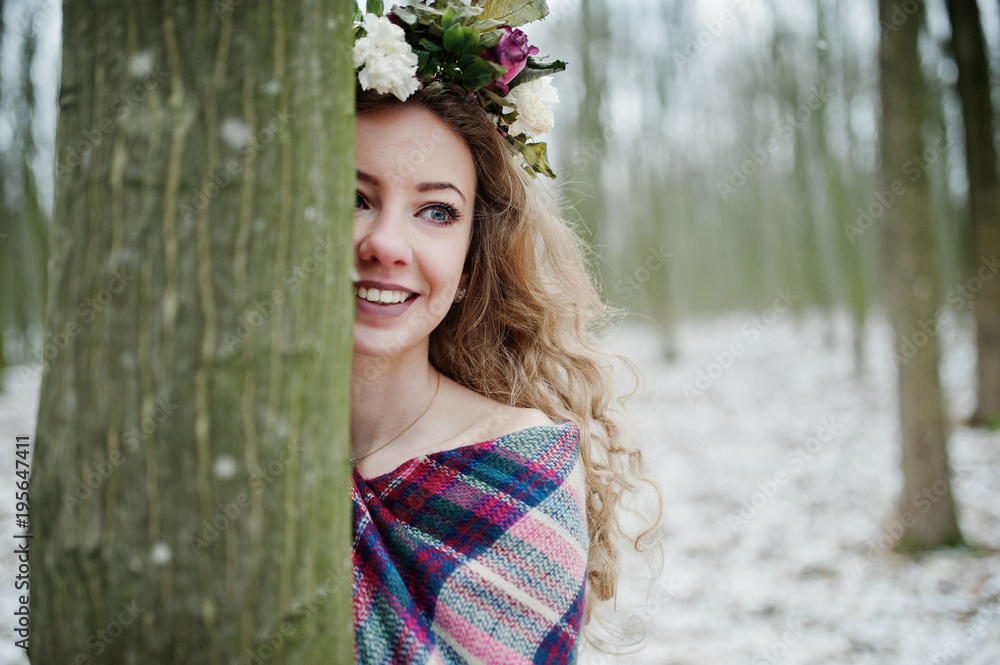 Curly cute blonde girl with wreath in checkered plaid at snowy forest in winter day. Curly cute blonde girl with wreath in checkered plaid at snowy forest in winter day.