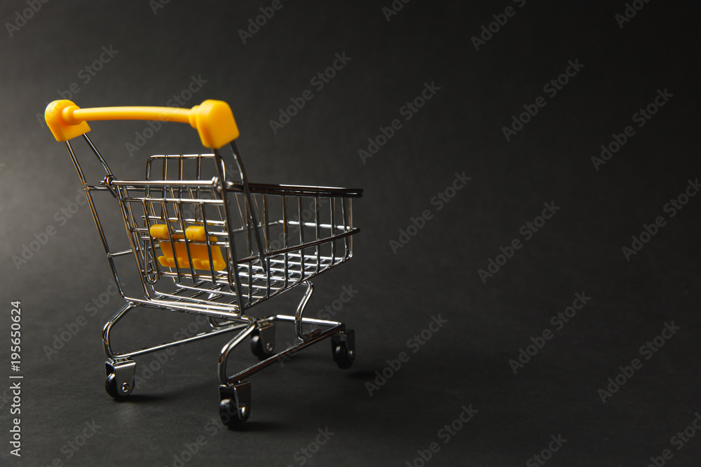 Close up of supermarket grocery push cart for shopping with black wheels and yellow plastic elements on handle isolated on black background. Concept of shopping. Copy space for advertisement Close up of supermarket grocery push cart for shopping with black wheels and yellow plastic elements on handle isolated on black background. Concept of shopping. Copy space for advertisement