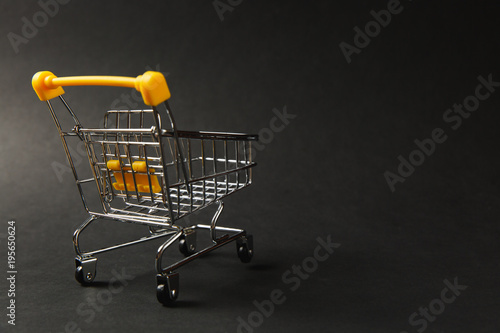 Close up of supermarket grocery push cart for shopping with black wheels and yellow plastic elements on handle isolated on black background. Concept of shopping. Copy space for advertisement