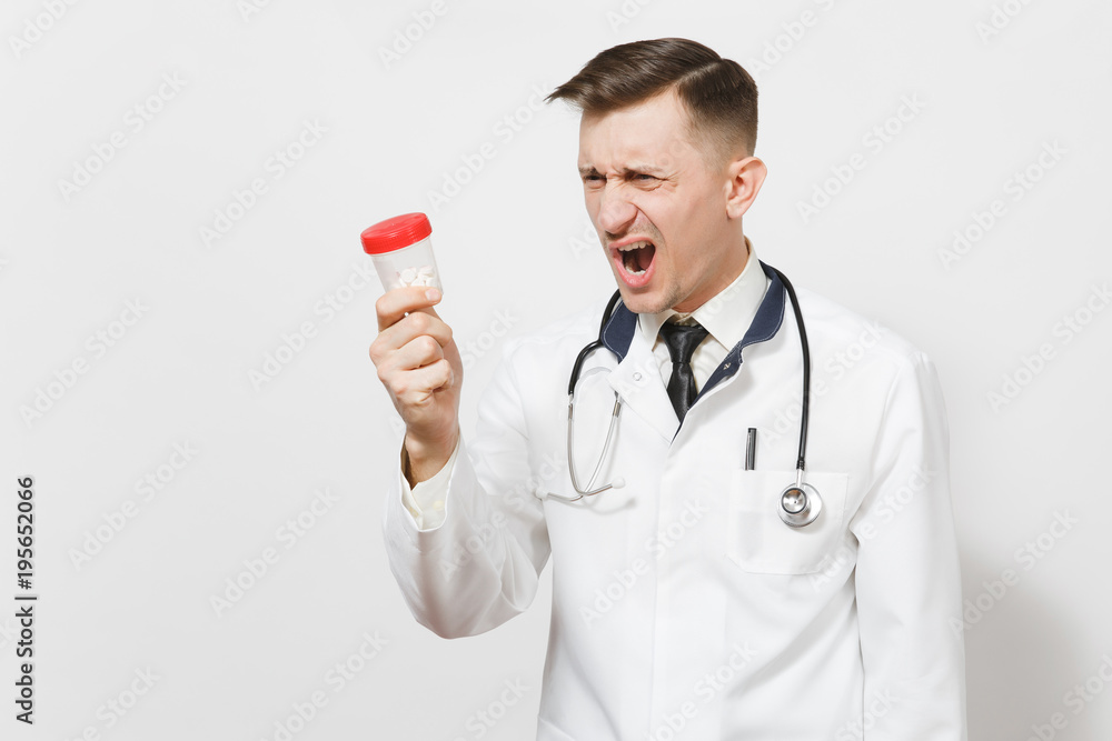 Angry screaming shocked young doctor man isolated on white background. Male doctor in medical uniform, stethoscope holding bottle with white pills. Healthcare personnel, health, medicine concept. Angry screaming shocked young doctor man isolated on white background. Male doctor in medical uniform, stethoscope holding bottle with white pills. Healthcare personnel, health, medicine concept.