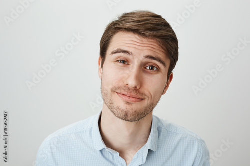 Studio portrait of attractive pleasant male office worker with tired expression, feeling sorry for his coworker who got in trouble, listening her story and nodding, smiling over gray wall