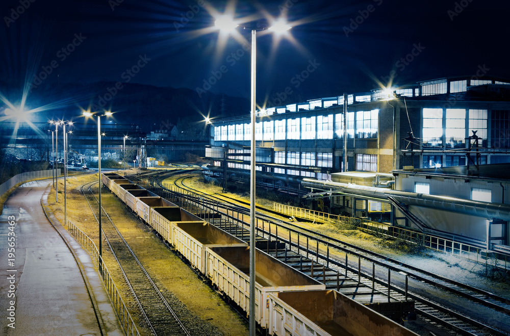 Industriebahnhof Rangierbahnhof bei Nacht mit vielen Lichtern und Waggons auf einem Abstellgleis in einer Industrieanlage mit violetter Optik