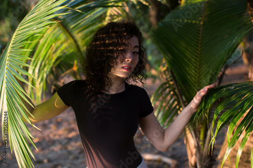 Beautiful asian girl looks through the palm leaves..