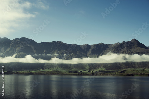 Paisaje de monta  as con picos nevados y nubes. Las monta  as se reflejan en un lago. Escena diurna  cielo azul y despejado. Nueva Zelanda.