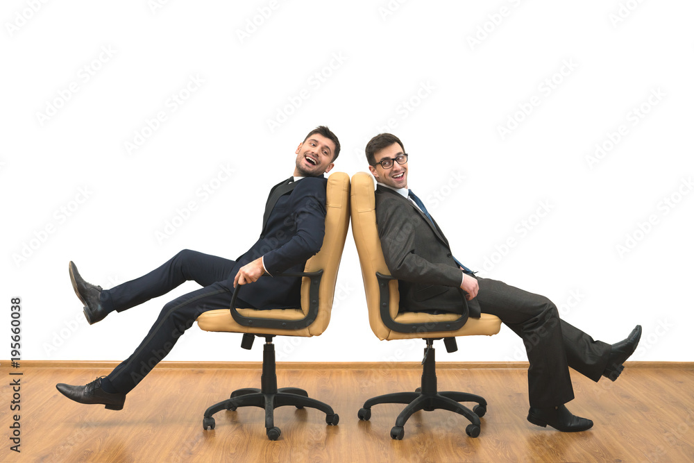 The two happy men sit on chairs on the white wall background The two happy men sit on chairs on the white wall background