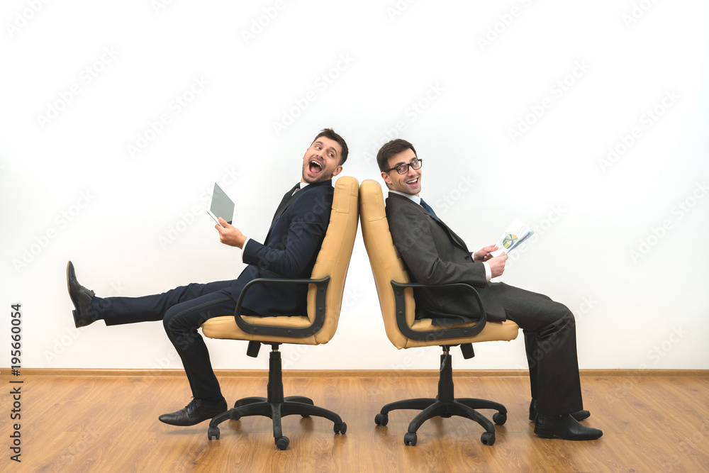 The two businessmen with a tablet and papers sit on the white wall background The two businessmen with a tablet and papers sit on the white wall background