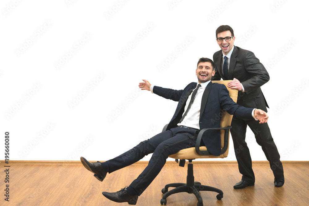 The two happy businessmen ride on the chair on the white wall background The two happy businessmen ride on the chair on the white wall background
