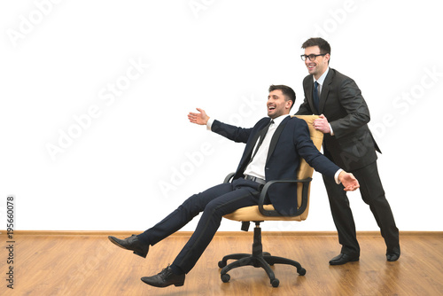 The two happy businessmen ride on the chair on the white wall background