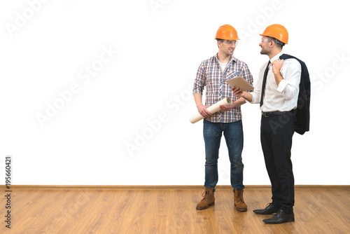 The two men in helmets stand with a tablet on the white wall background