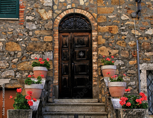 Old wooden door decorated with flowerpots and steps in medieval town, Tuscany, Italy