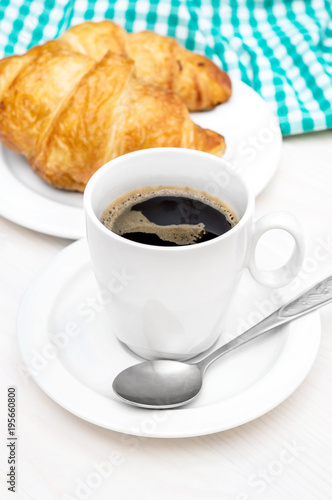 Cup of coffee and plate with croissants on the white table.