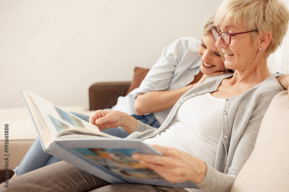 Mother and daughter having a great time while looking through old family photo album. Happy family moments at home Mother and daughter having a great time while looking through old family photo album. Happy family moments at home