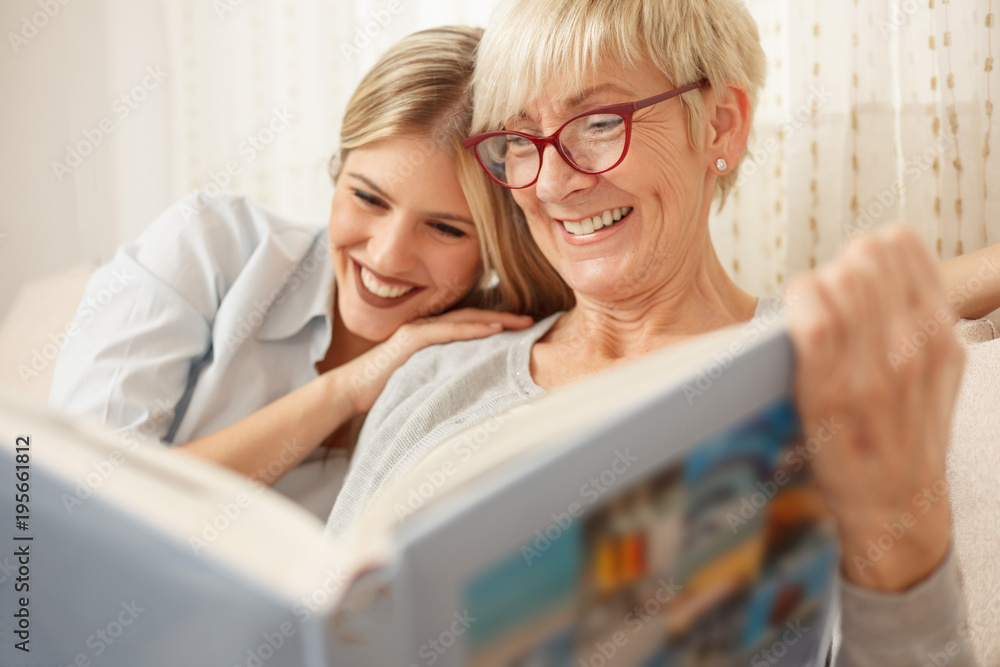 Mother and daughter having a great time while looking through old family photo album. Happy family moments at home