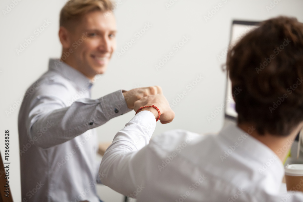 Obraz premium Smiling male colleagues fist bumping at workplace, happy friends greeting, partners sharing success, employees celebrating good teamwork result, workers supporting motivation concept, close up view