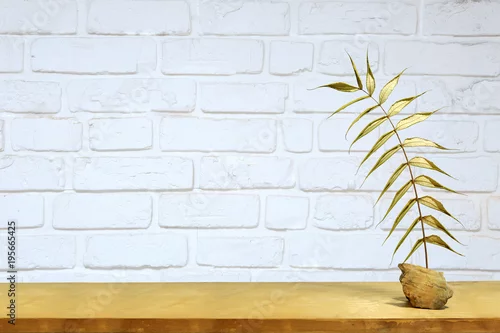 Obraz Złoty liść na półce na tle białej ścianie z cegły.