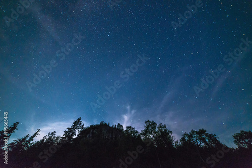 Milky way and starry sky with wispy clouds along a steep cliff at night © claire
