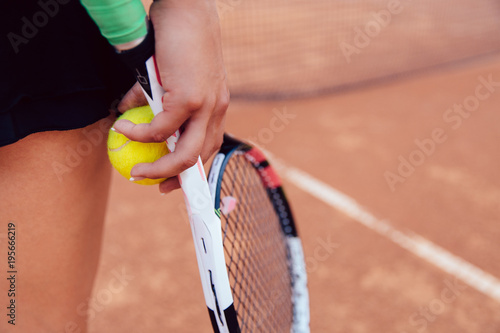 Woman holding tennis racket and ball on clay court. Close-up. Sport concept. © Maksym Azovtsev