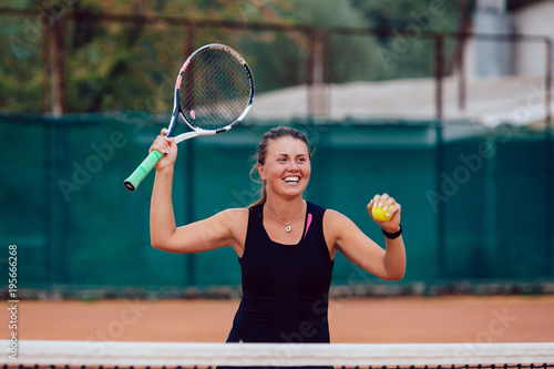 Tennis player. Cheerful beautiful girl playing tennis, prepares to serve a tennis ball. Dressed in black t-shirt. © Maksym Azovtsev