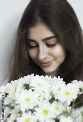 A beautiful girl with black hair looks at a bouquet of white flowers. A young woman received flowers from her beloved. 
