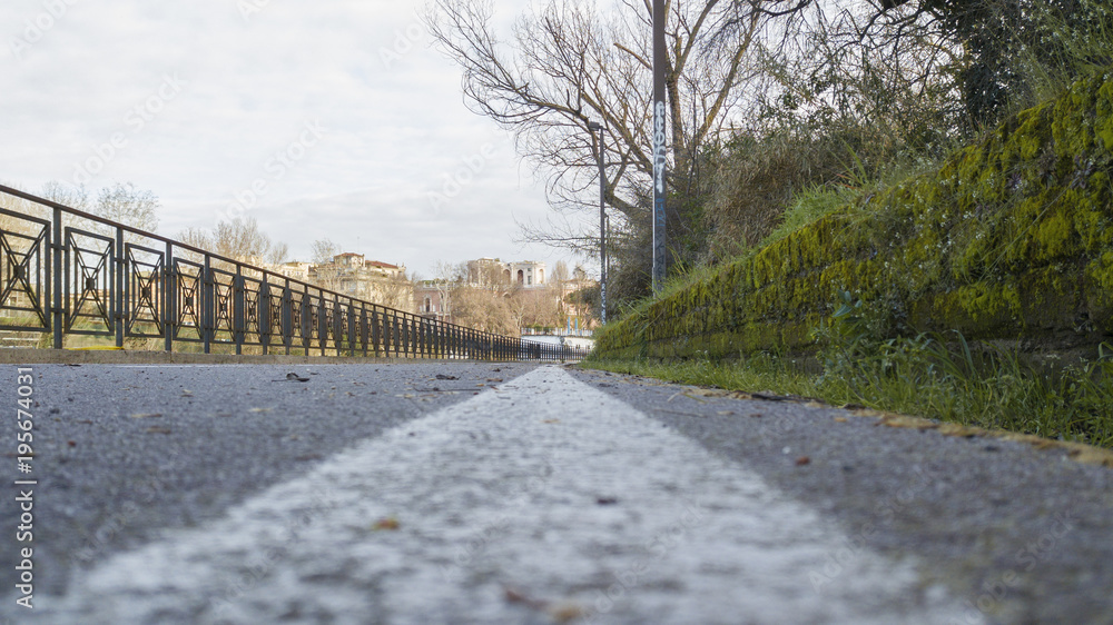 View from the bottom of an asphalt road with trees and vegetation on the sides and on the left a railing that separates from the river. View from the bottom of an asphalt road with trees and vegetation on the sides and on the left a railing that separates from the river.
